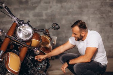 Bir adam garajda motorsikletinin tozunu alıyor.