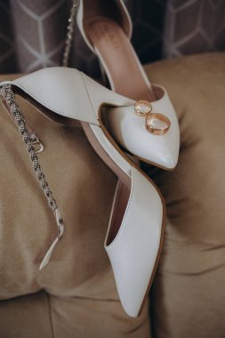 Gelinin ayakkabıları ve alyansı cam bir masada. Geleneksel gelin aksesuarları, yüksek topuklu beyaz ayakkabılar ve alyans şeklinde. Yüksek kalite fotoğraf