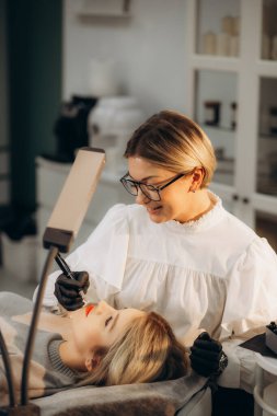 Kozmetik uzmanı bir kadının yüzünde kalıcı makyaj yapıyor. Uzman hastanın dudaklarına yakın plan bir dövme uygular. Yüksek kalite fotoğraf