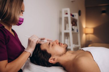 Kozmetik uzmanı spa salonunda adamın yüzüne maske takıyor.