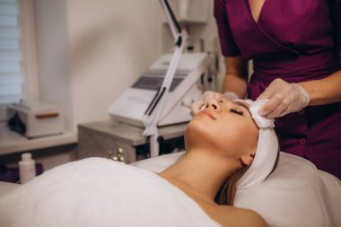 İnsanlar, güzellik, kaplıca, kozmetik ve rahatlama konsepti. Kapalı gözlerle uzanan ve kaplıcada yüz temizliği yaptıran güzel bir genç kadına yakın çekim. Yüksek kalite fotoğraf