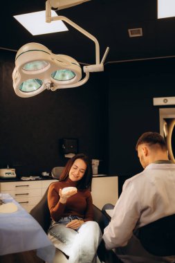 Bir kadın göğüs implantı tutuyor ve bir estetik cerrahla konuşuyor.