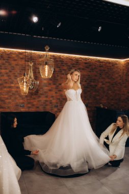 Gelinlik mağazasında gelinlik için gelinlik seçiyor ve tasarımcı ona yardım ediyor. Yüksek kalite fotoğraf