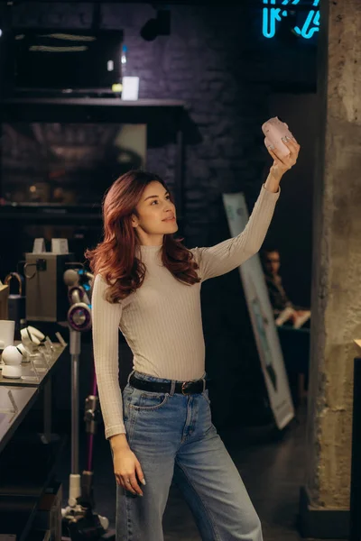 Bir kadın elektronik mağazasında fotoğraf makinesinde selfie çekiyor.