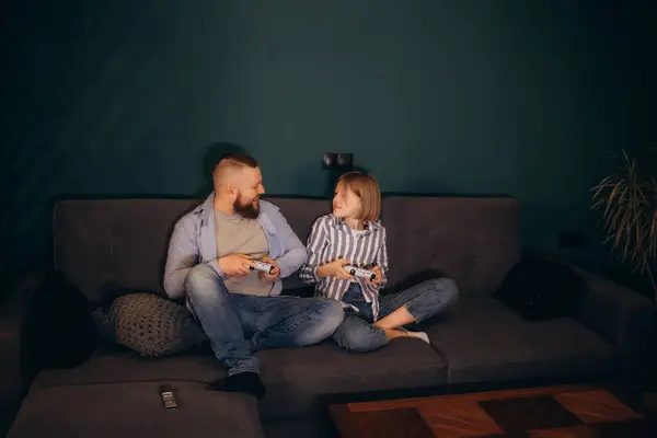 family, gaming and entertainment concept - happy father and little daughter with gamepads playing video game at home. High quality photo