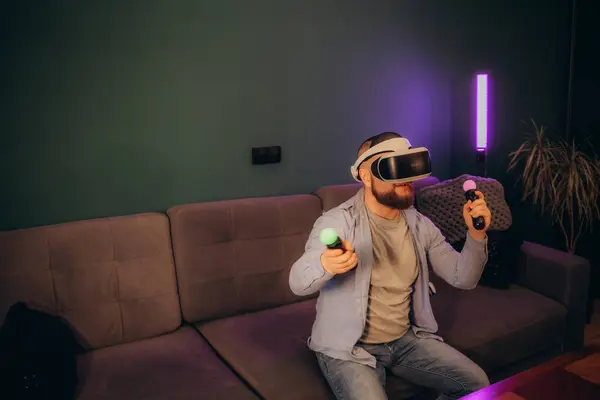 technology, gaming, entertainment and people concept - happy young man with virtual reality headset or 3d glasses with controller gamepad playing racing video game at home. High quality photo
