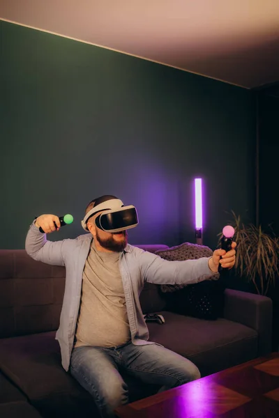 technology, gaming, entertainment and people concept - happy young man with virtual reality headset or 3d glasses with controller gamepad playing racing video game at home. High quality photo