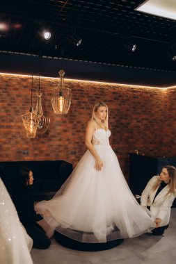 Güzel gelin düğün gününde en iyi arkadaşı tarafından giydiriliyor ve dükkanda bir gelinlik seçiyor ve tezgahtar da ona yardım ediyor. Yüksek kalite fotoğraf