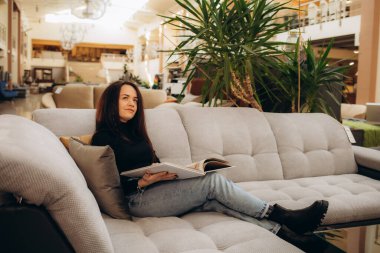 Bir kadın mobilya mağazasında otururken kanepe kataloğuna bakar.