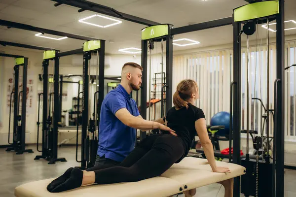 Spor sakatlığı sonrası fizyoterapi sırasında sırt bükme egzersizi yapan genç bayan sporcuların yan görüntüsü. Sağlık merkezi uzmanı travmadan sonra kadının esnekliğini geri kazanmasına yardım ediyor. Yüksek kalite fotoğraf