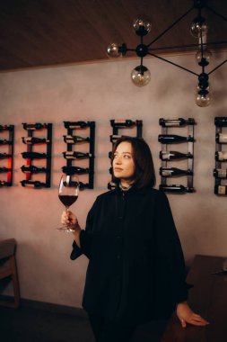 Woman in the wine cellar with barrels in background drinking and tasting wine.