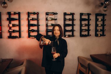 Kadın barmen tatmak için bardağa beyaz şarap dolduruyor.