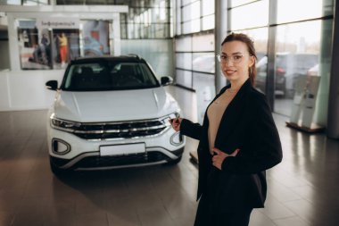 Portrait of salesperson in car showroom. Attractive young woman stend in front of car. Beautiful woman in suit in front of luxury car