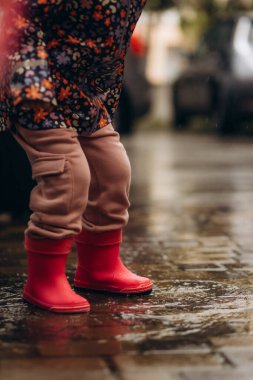 Sarı lastik çizmeli bir çocuğun ayakları yağmurda su birikintisinin üzerinden atlıyor..