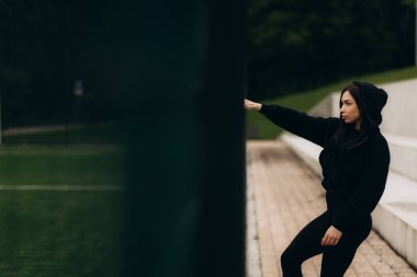 Futbol sahasının yanında koyu renk spor giyimli bir kadın.