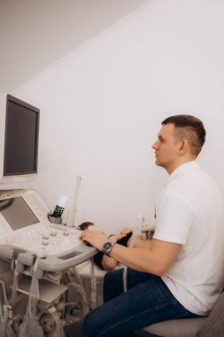 Sakallı esmer bir doktorun modern usg aletine dokunuşunun yan görüntüsü. Teşhis prosedürünü başlatıyor. Profesyonel radyolog mavi cübbe giyen küçük çocuk için ultrason taraması yapıyor.. 