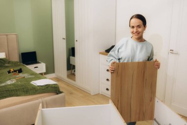 Güzel, genç ve mutlu bir kadın evde mobilya monte ediyor.