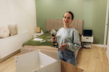 Güzel, genç ve mutlu bir kadın evde mobilya monte ediyor.