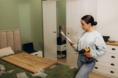 Mobilya montajı için elinde elektrikli tornavida tutan ve kullanma kılavuzu okuyan kadınlar.