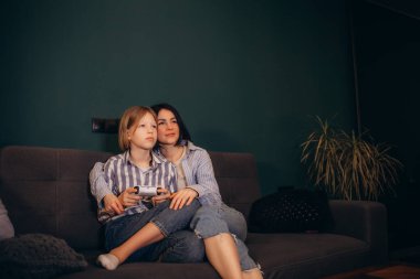 Anne ve kızı kanepede televizyon izliyor.