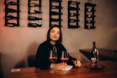 Kadın profesyonel şarap garsonu masaya oturup kırmızı ve beyaz şarabı tadıyor ve şarap bardaklarına dökülüyor ahşap bir rafın arka planında..