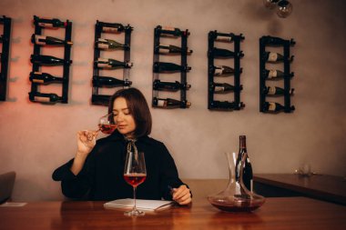 Esmer kadın şarap tadıyor, şarap içiyor ve notlar yazıyor..