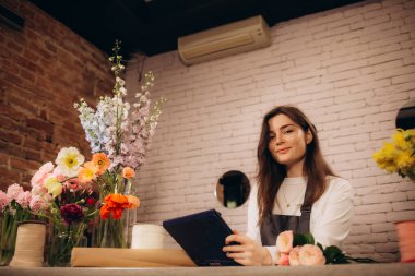 Bir dost ve misafirperver çiçekçi iş kadını sahibi portre gururla bir dizüstü bilgisayar kullanarak bir çiçek mağazasının tezgahında ayakta, gülümseyerek. Küçük işletme teknolojisi.