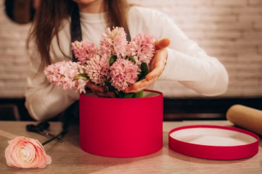 Paket kağıdında çiçek buketi. Genç güzel çiçekçi kız çiçekçiyi pembe şakayık ve kır çiçekleriyle ahşap arka plandaki atölyede birleştiriyor. Kadın eli iş başında.