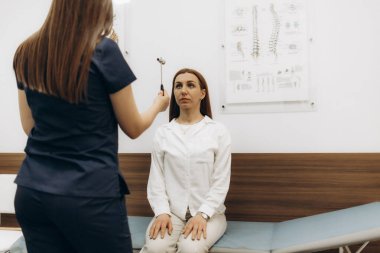 Neurologist doctor with special hammer checking eye reflexes of young female patient in hospital 