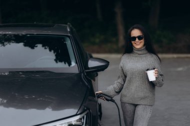 Kadın elektrikli arabasını şarj tabancasıyla dolduruyor.