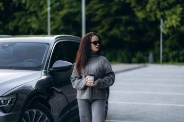 Progressive woman install cable plug to her electric car with home charging station. Concept of the use of electric vehicles in a progressive lifestyle contributes to clean environment.