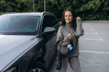 Güzel başarılı Avrupalı kız şehirdeki şarj istasyonunda elektrikli cipini şarj ediyor. Elektrikli araba, geleceğin ulaşım aracı..