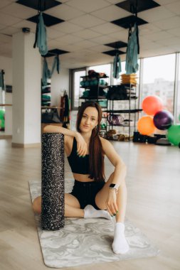 Egzersiz için köpük silindiri kullanıyorum. Zayıf vücutlu genç bir kadın stüdyoda spor kıyafetleri giyiyor..