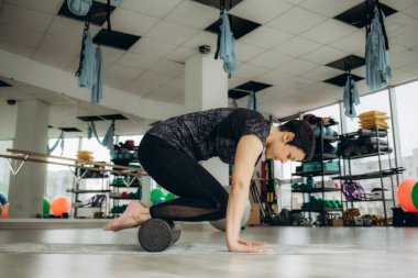 Esneme egzersizleri yaparken köpük silindiri kullanan genç bir kadın.