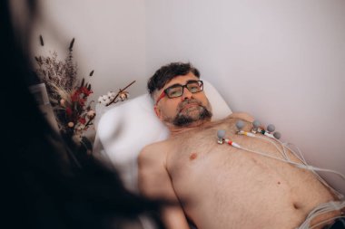 Kadın doktor hemşire yaşlı bir adama EKG testi yapıyor..