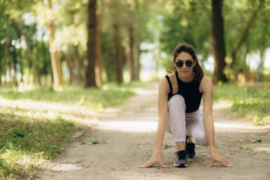 Fitness kadın koşucusu dışarıda başlangıç pozisyonunda. Parkta koşan bir kadın. Sportif kadın koşmadan önce alçakta duruyor. Koşu, açık hava eğitimi, aktif yaşam tarzı kavramı.