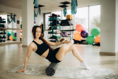 Spor yapan kadın esneme hareketleri, ısınma hareketleri, köpük silindiri kullanarak pilates egzersizleri yapıyor.