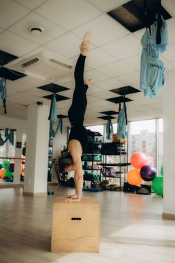 Kız yoga stüdyosunda eğitim görüyor. Bej eşofman giyip duvara karşı amuda kalkıyor. Sağlıklı yaşam tarzı ve yoga konsepti.