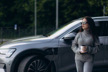 Elektrikli benzin istasyonunda kadın elektro arabayı şarj ediyor.