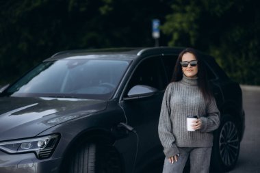 Elektrikli benzin istasyonunda kadın elektro arabayı şarj ediyor.