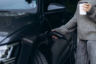 Kadın elektrikli arabasını şarj tabancasıyla dolduruyor.