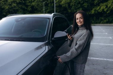 Halka açık bir istasyonda elektrikli arabasının yanında duran genç bir kadının portresi. Modern yaşam tarzı ve başarı kavramı