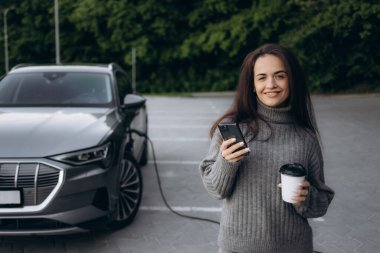 Elektrikli benzin istasyonunda kadın elektro arabayı şarj ediyor.