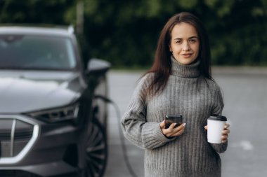 Elektrikli benzin istasyonunda kadın elektro arabayı şarj ediyor.