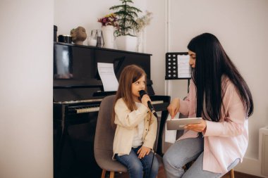 Bir bayan öğretmen küçük bir kıza müzik okulunda şarkı söylemeyi öğretiyor.