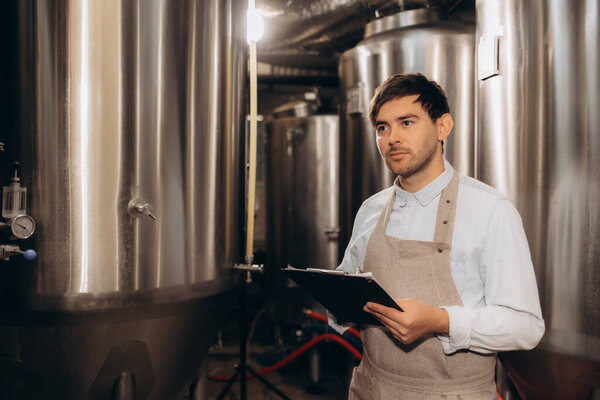 Man working in craft brewery examining production of the beer.