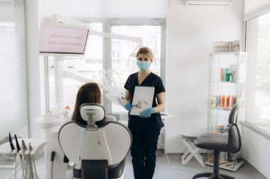 Kadın bir dişçi, ofiste bir hastayla iletişim kurar.