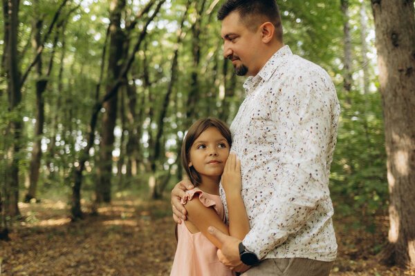 A father hugs his daughter while walking in the forest