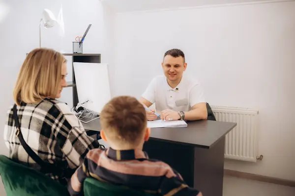 stock image Happy young Caucasian male doctor give high five to cute small 7s boy patient at consultation with mom in hospital. Smiling pediatrician make deal cheer little kid child in clinic