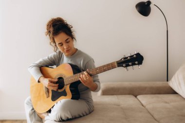 Yaratıcı hobi. Yetenekli, genç, melez, bayan müzisyen koltuğuna tek başına oturmuş klasik gitar kullanarak enstrümantal bir şarkı besteliyor. Gülümseyen melez kadın müzik aletinde sakin bir melodi çalar. Boşluğu kopyala